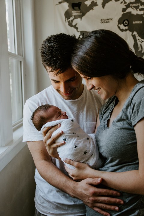 Das Bild zeigt junge Eltern, die ein Neugeborenes halten.