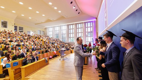 Man sieht, wie Prof. Lasch den Absolvent:innen ihre Rosen überreicht.