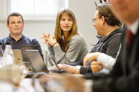 Zu sehen ist ein meeting, bei dem sich drei Menschen unterhalten