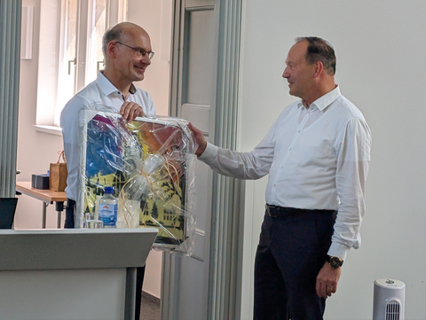 Zu sehen ist Prof. Udo Buscher, der ein Geschenk an Prof. Rainer Lasch übergibt.