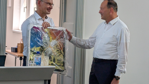 Zu sehen ist Prof. Udo Buscher, der ein Geschenk an Prof. Rainer Lasch übergibt.