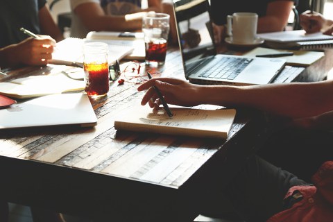 Man sieht einen Tisch, auf dem Notizbücher liegen und Getränke stehen