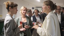 Es ist eine Gruppe von Menschen bei einer Festveranstaltung zu sehen, die sich unterhalten