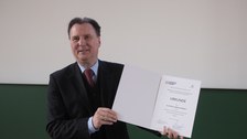 Es ist der Dekan zu sehen mit einer Urkunde in der Hand