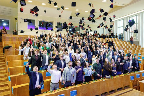 Die Absolvent:innen werfen ihre Graduiertenhüte in die Luft für das bekannte Hutwerffoto. 