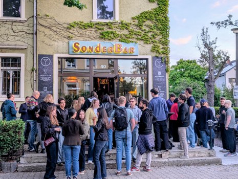 Zu sehen ist eine große Gruppe junger Menschen vor der SonderBar