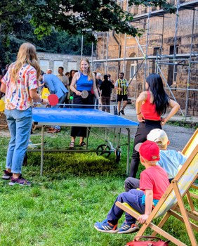 Zu sehen sind junge Menschen, die Tischtennis spielen und zwei kleine Kinder, die zuschauen