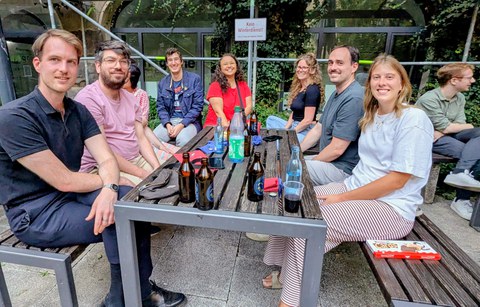 Zu sehen sind junge Menschen, die an Tischen sitzen bei einem Grillfest