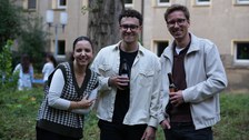 Es sind drei junge Menschen bei einem Grillfest zu sehen