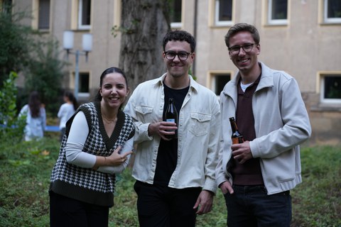 Es sind drei junge Menschen bei einem Grillfest zu sehen