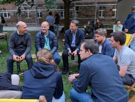 Es sind Menschen auf einem Fest zu sehen, die in Liegstühlen sitzen und sich unterhalten