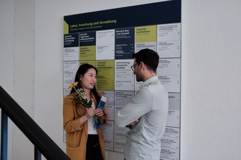 Zu sehen sind zwei junge Menschen, die sich vor einer Infotafel unterhalten 