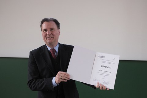 Es ist der Dekan zu sehen mit einer Urkunde in der Hand