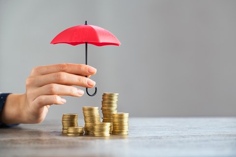 Zu sehen ist eine Hand, die einen roten Regenschirm über einige Stapel mit Münzen hält 