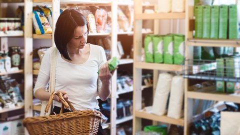 Es ist eine Frau in einem Lebensmittelgeschäft zu sehen, die sich ein Produkt näher anschaut 