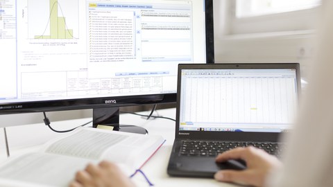 Zu sehen ist ein Laptop und ein großer Bildschirm mit dem Programm SPSS