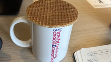 Zu sehen ist eine Tasse auf der ein Keks liegt 