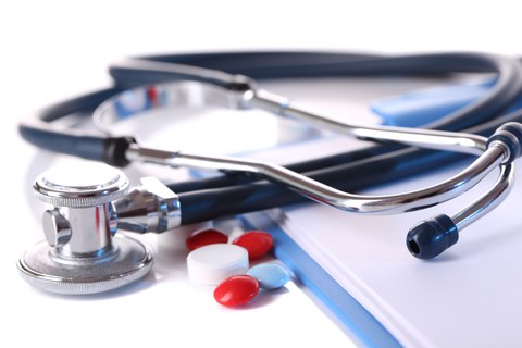 Es sind ein Stetoskop zu sehen und Pillen, die auf einer Krankenakte liegen.
