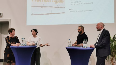 Zu sehen sind vier Menschen, die bei einer Paneldiskussion sind. 