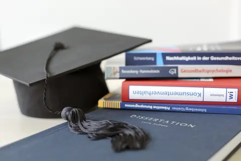 You see a dissertation, a stack of books and a doctoral hat