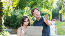 Foto von zwei Personen im Freien, die ein Laptop halten. Der Mann zeigt auf etwas vor ihnen.