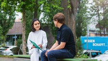 Ein Mann und eine Frau lernen zusammen und sitzen auf einer Bank im Park des Hörsaalzentrums.
