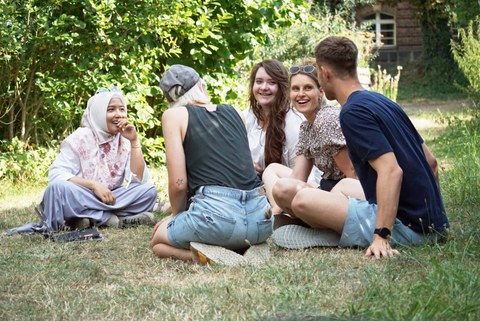 Foto von 5 Personen, die auf einer Wiese auf dem Campus der TU Dresden sitzen und sich unterhalten.