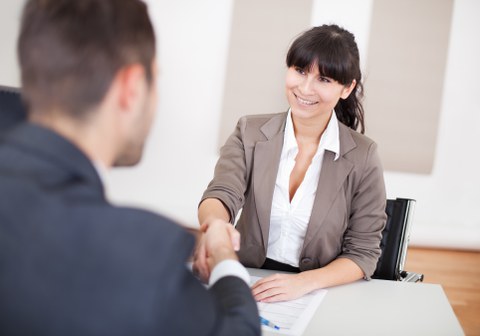 Das Foto zeigt zwei Personen in Businesskleidung. Sie sitzen an einem Tisch und geben sich gerade die Hand. Zwischen ihnen liegt ein Dokument.