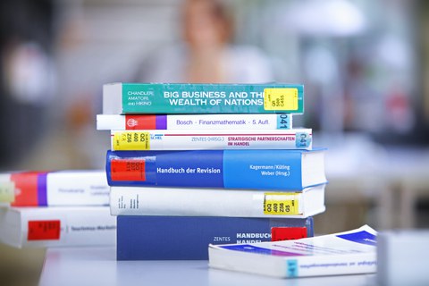 Das Foto zeigt eine Stapel Bücher aus der Bibliothek zum Thema Handel und Finanzen. Sie liegen übereinander auf einem Tisch.