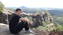 Foto: Ein Student sitzt in der sächsischen Schweiz auf einer Anhöhe und blickt lächelnd in die Kamera