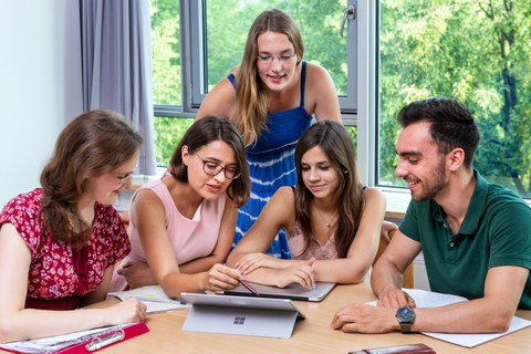 Foto von fünf Studenten, die in einer Workshoprunde zusammen am Laptop lernen.