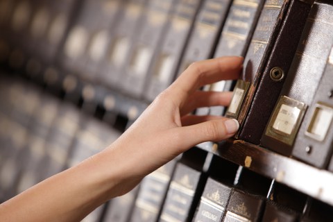 Die Hand einer Frau holt ein Buch aus einem Archivregal in einer Bibliothek.