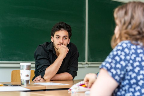 Foto: Ein Mann und eine Frau sitzen sich an einem Tisch gegenüber. Er hört ihr zu