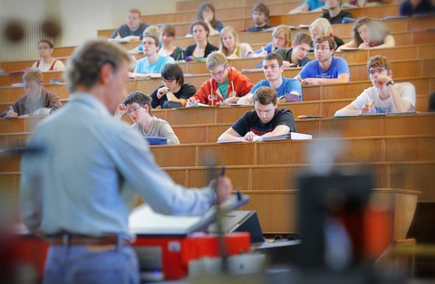 Das Foto zeigt einen Dozenten im Vordergrund mit Blick auf seinen Kurs. Die Studierenden stehen im Fokus. Viele schauen nach vorn oder machen sich Notizen. 