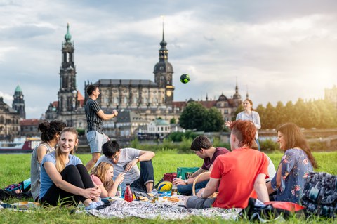 Gruppe von Studenten an der Elbe. Sie spielen Volleyball und sitzen plaudernd auf der Wiese