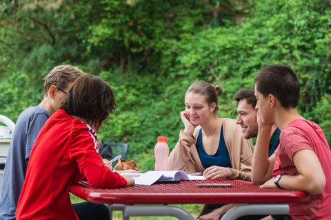 Foto von fünf Studenten, die am Imbisstisch am Hörsaalzentrum sitzen und zusammen lernen.