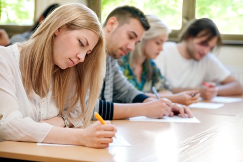 Photo of four students sitting side by side at a table and writing something.