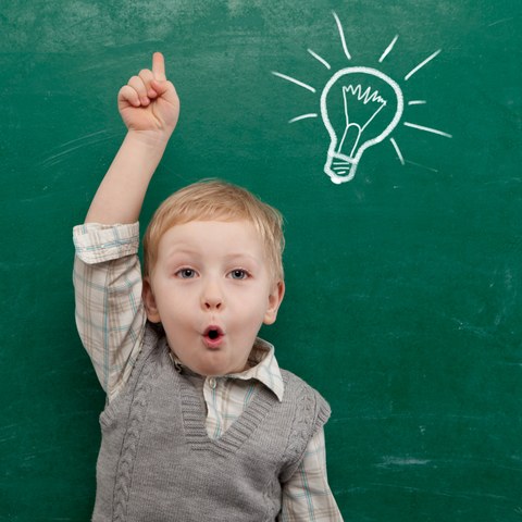 Child with a raises hand in front of a blackboard on which a light bulb is drawn.