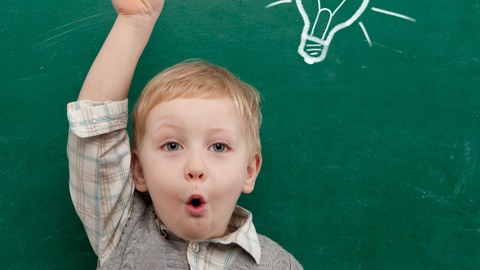 Child with a raises hand in front of a blackboard on which a light bulb is drawn.