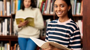 Es sind zwei Studentinnen zu sehen in einer Bibliothek