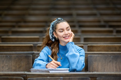 Foto einer Studierenden, die glücklich lächelnd im Hörsaal sitzt.