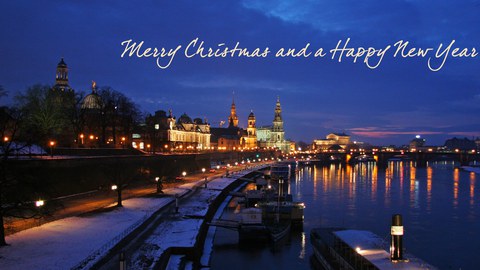 Foto der Dresden Silhouette mit Blick auf Elbe in Richtung Semperoper in weihnachtlich beleuchteter Abendstimmung mit spiegelnden Lichtern im Fluss und dem Schriftzug in Schreibschrift: "Merry Christmas and a Happy New Year!" 