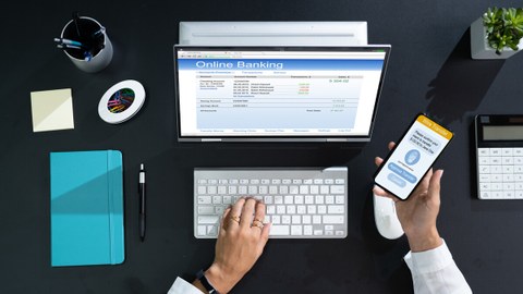 Bild zeigt eine Person, die an ihrem Schreibtisch am Laptop sitzt und sich per 2-Faktor Anmeldung beim Online Banking anmeldet.