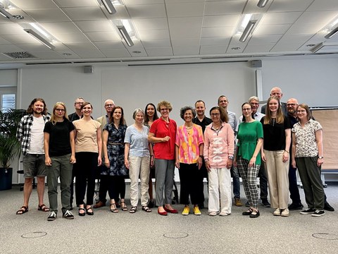Gruppenfoto des Treffens, es sind 19 Personen vor einer Leinwand zu sehen