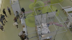 Blick von oben auf einen Ausstellung mit Gerüstelementen und ca. 15 Besuchenden