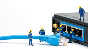 Fotorealistische Darstellung von 6 Miniatur-Handwerkern in blauer Arbeitskleidung und Helm vor einem LAN-Stecker, der offenbar angeschlossen werden soll.. 