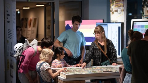 Foto von 2 Kindern und mehreren erwachsenen Personen an einem interaktiven Ausstellungsmodul im COSMO Wissenschaftsforum