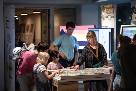 Foto von 2 Kindern und mehreren erwachsenen Personen an einem interaktiven Ausstellungsmodul im COSMO Wissenschaftsforum