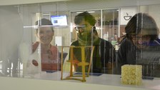 Foto von drei Gesichtern in Betrachtung der Ausstellungsexponate (im Vordergrund) durch die Vitrine hindurch fotografiert.