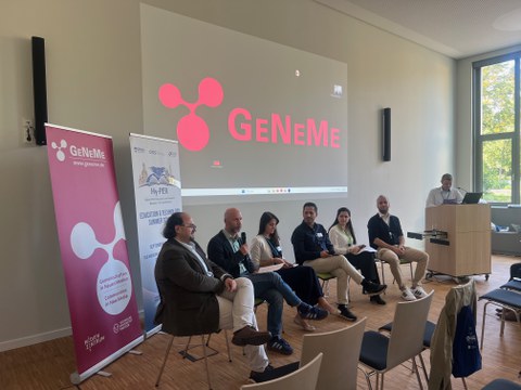 Fotoaufnahme der Podiumsdiskussion von Hy-PER 2026 mit 7 Personen im Podium an der Wand dahinter das Logo der GeNeMe als Projektion